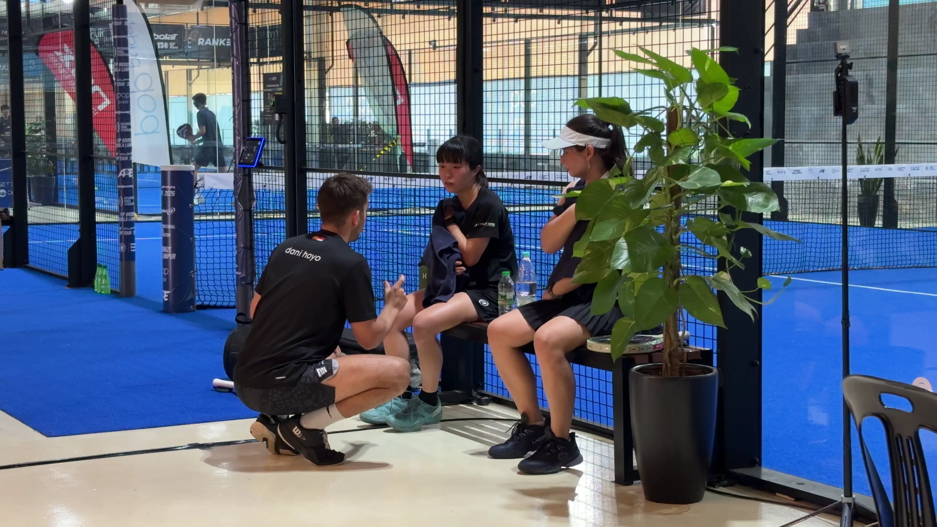 Dani talking with Chifumi Sato and another player between points, on a blue padel court