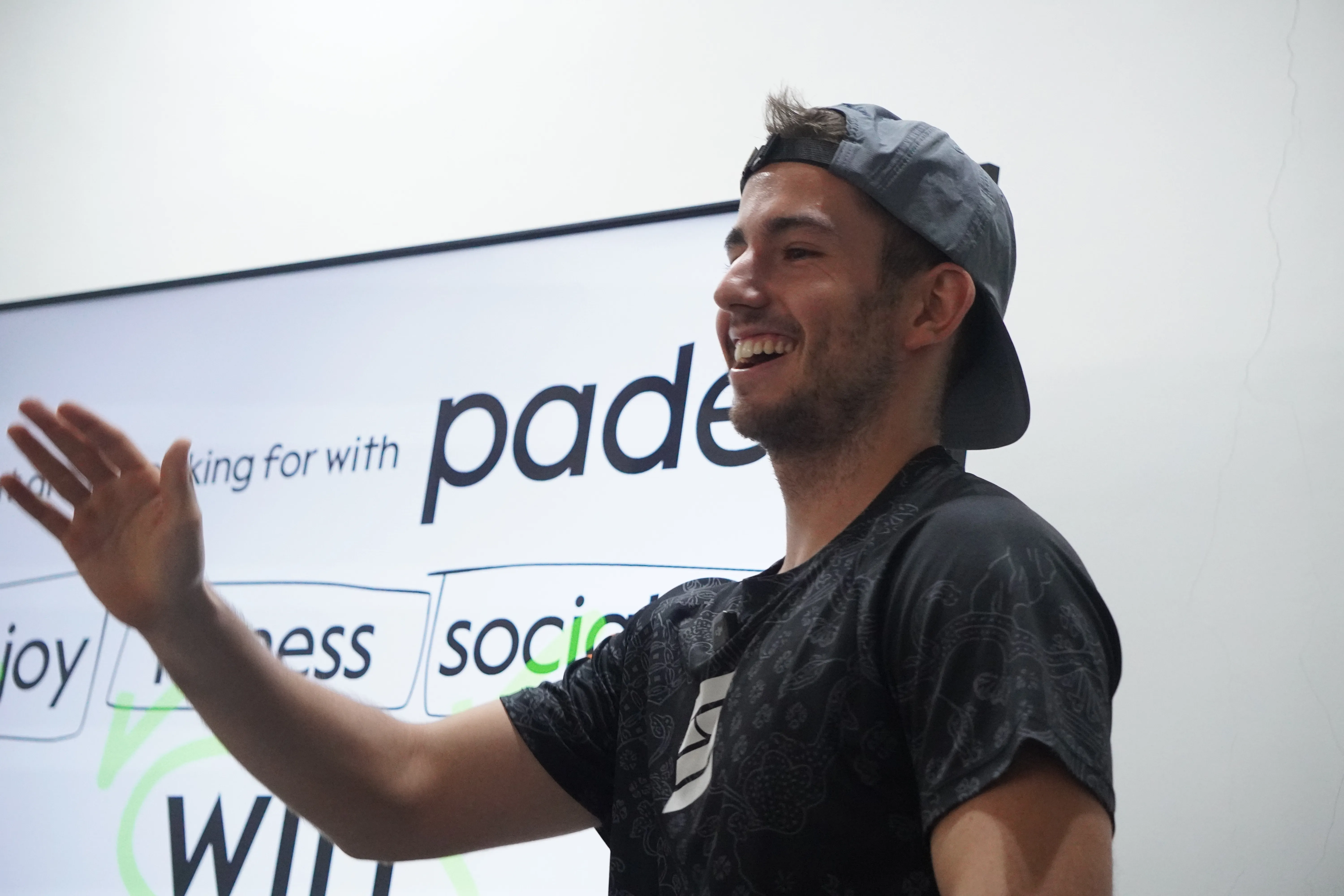Dani teaching a class, laughing, in front of a screen that reads "what are you looking for with padel".