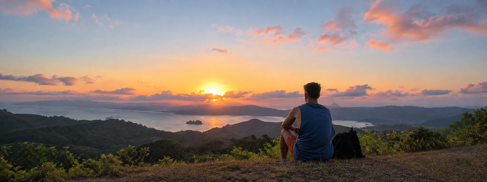 A player sitting on a hill in Lombok, looking at the sunset over the sea